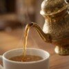 Brass_kettle_pouring_tea_202607121054 Royal Handcrafted Pure Brass Tea Kettle (Teapot / Ketli) – Vintage Antique Finish with Floral Relief Engravings, Swan Spout & Pedestal Base