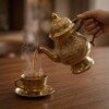 Brass_kettle_pouring_tea_cup_202607121054 Royal Handcrafted Pure Brass Tea Kettle (Teapot / Ketli) – Vintage Antique Finish with Floral Relief Engravings, Swan Spout & Pedestal Base