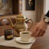 Hand_reaching_for_cup_202607121054 Royal Handcrafted Pure Brass Tea Kettle (Teapot / Ketli) – Vintage Antique Finish with Floral Relief Engravings, Swan Spout & Pedestal Base